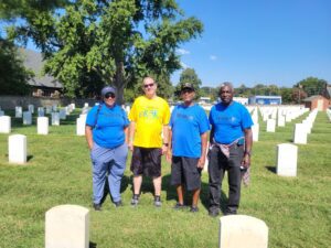 A group of four individuals standing in a cemetery, wearing Eggleston and veteran-themed t-shirts.